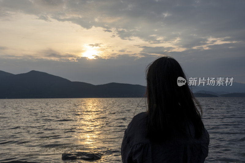 女子面朝湖水背朝夕阳的剪影画面