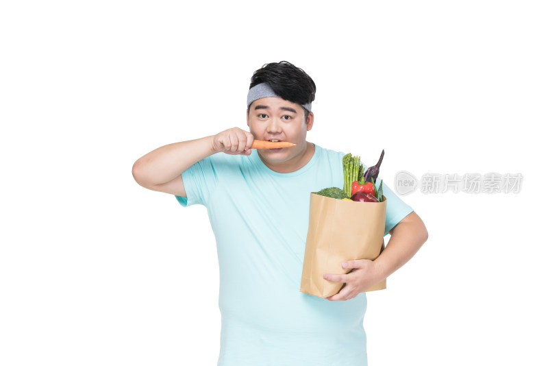肥胖的年轻男子拿着各种蔬菜在吃胡萝卜