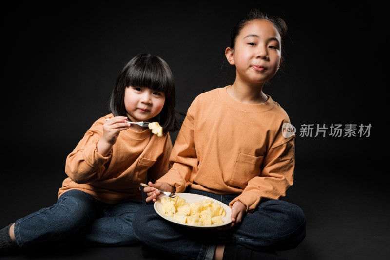 坐在黑背景前吃水果的两个亚裔女孩