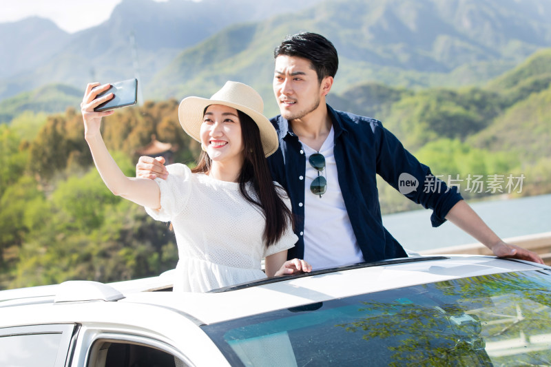 青年夫妇站在汽车上用手机拍照