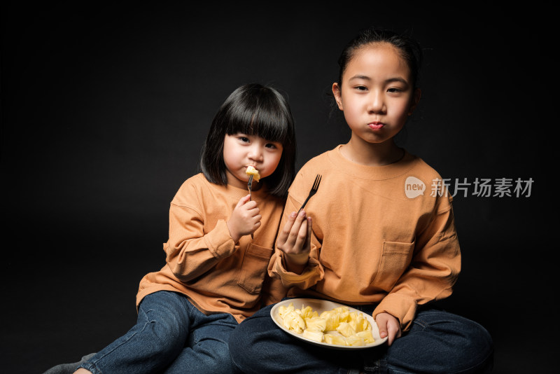 坐在黑背景前吃水果的两个亚裔女孩