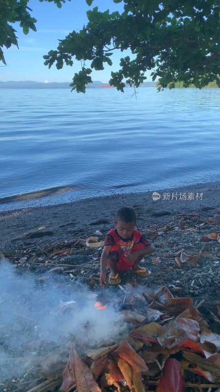 印尼当地小男孩在海边沙滩上生火