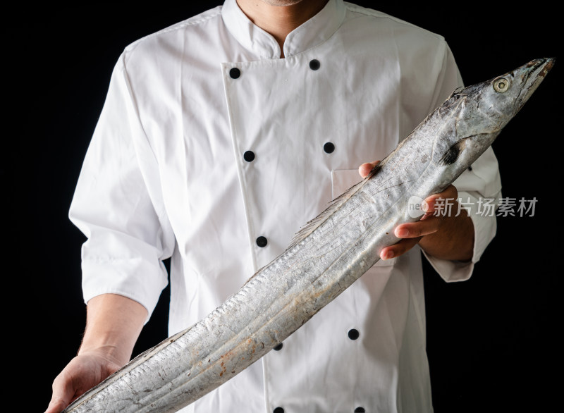 黑色背景前厨师拿着一条新鲜的带鱼