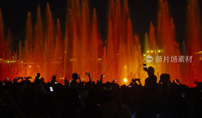 喷泉下高举手机欢呼的人群剪影