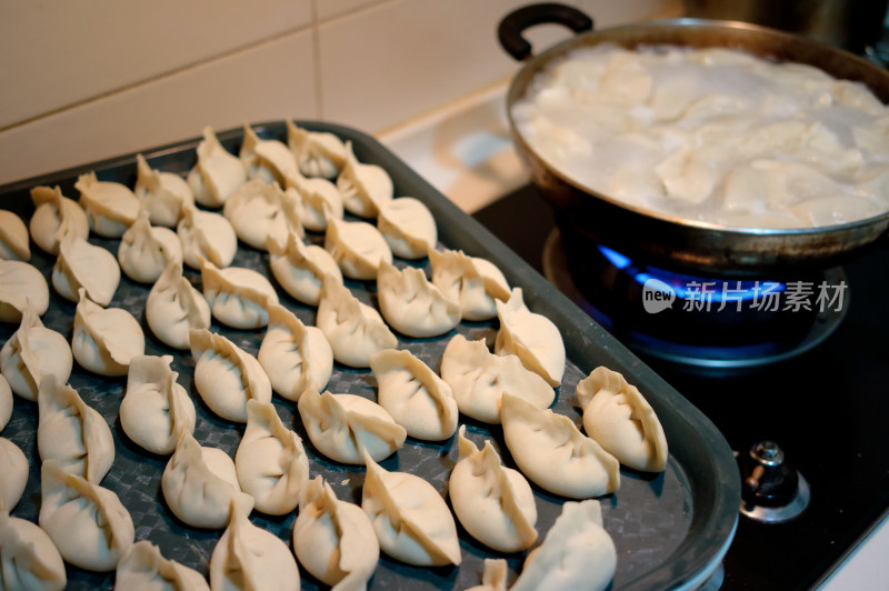 厨房灶台上煮水饺和待下锅的饺子