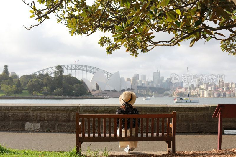 坐在长椅上看悉尼歌剧院的女人的后视图