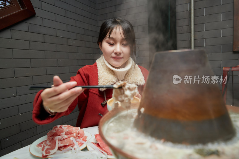 在饭店吃传统铜锅涮肉的亚洲少女