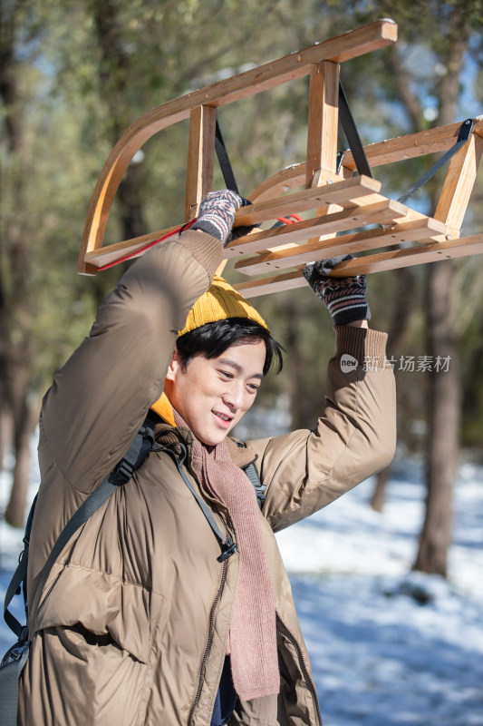 雪地上步行举着雪橇的青年男人