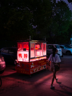 女子路过夜晚路边售卖鸭脖的小吃摊