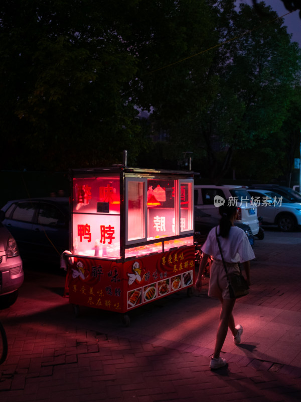 女子路过夜晚路边售卖鸭脖的小吃摊