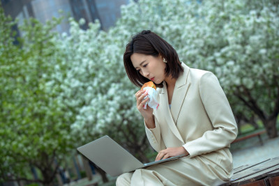 商务女士在户外边吃饭边用电脑