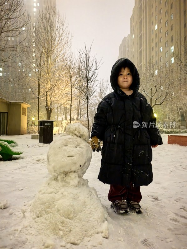 小孩雪地旁站立与雪人合影