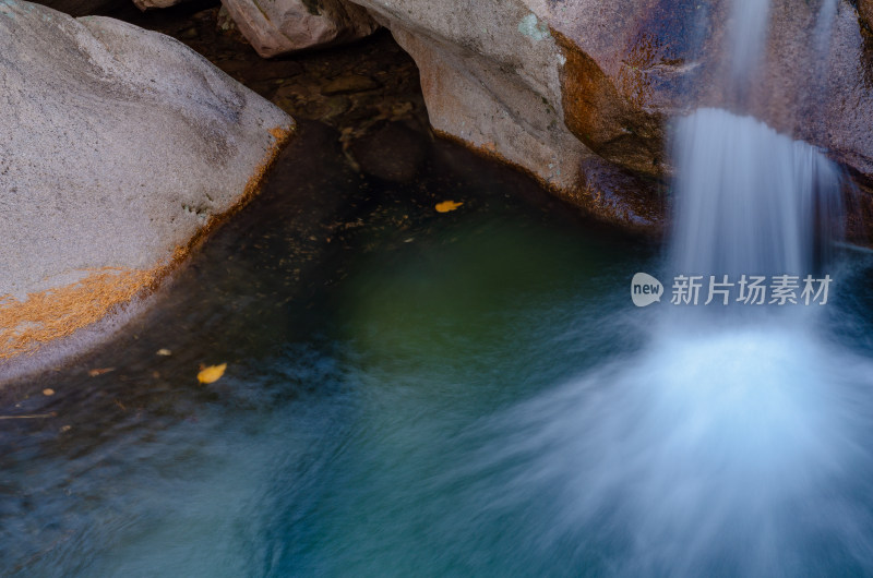 瀑布流到潭水中，水面上漂浮着几片黄叶