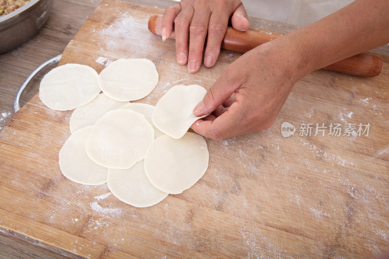 特写拍摄手拿擀面杖在砧板上擀饺子皮