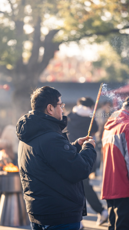 男子身着冬装户外上香的场景