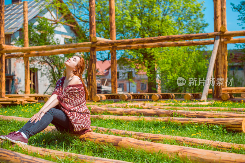 女子户外草地上坐木头上仰头
