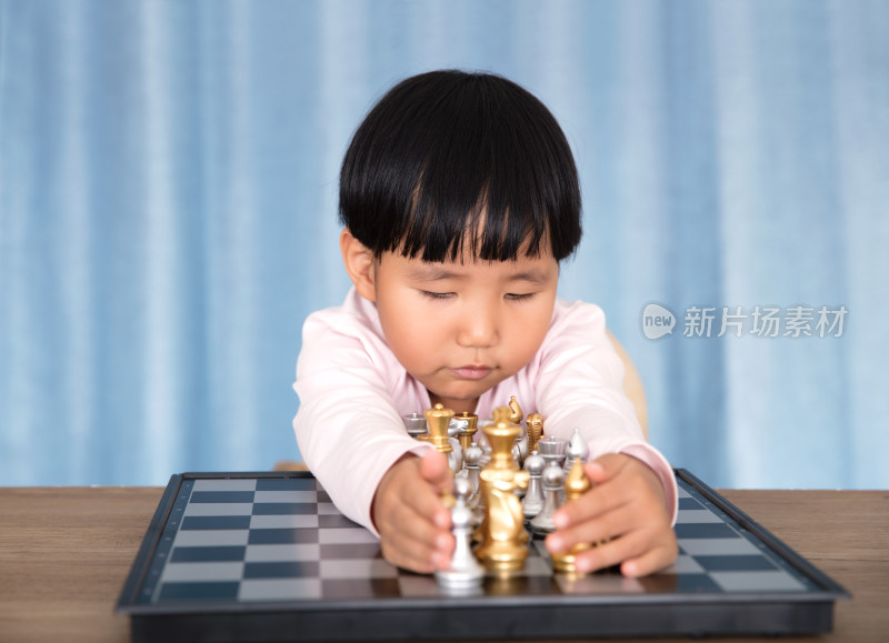 中国小孩子双手抱着国际象棋棋盘上的棋子