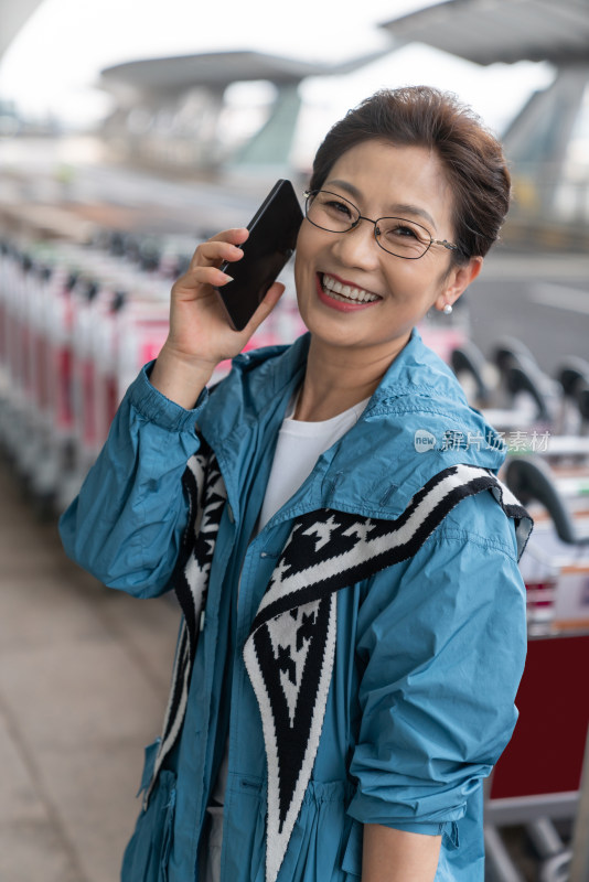 老年女人在机场拉着行李箱打电话