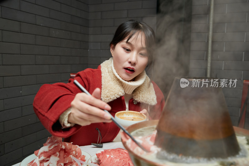 在饭店吃传统铜锅涮肉的亚洲少女