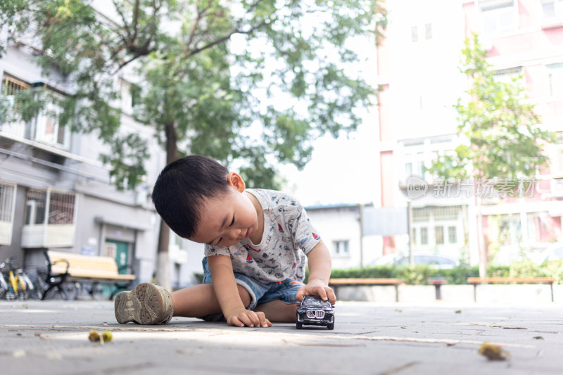 一个小男孩坐在院子里玩玩具车