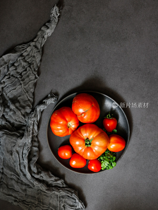 黑色桌面上，盘子中的新鲜蔬菜西红柿番茄