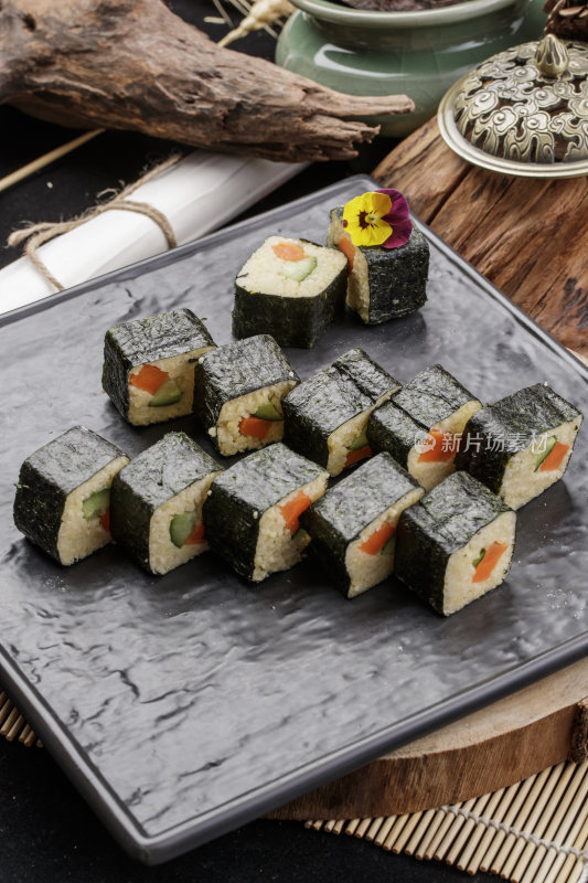 黑色石盘装的小米寿司卷摆放在樟木砧板上