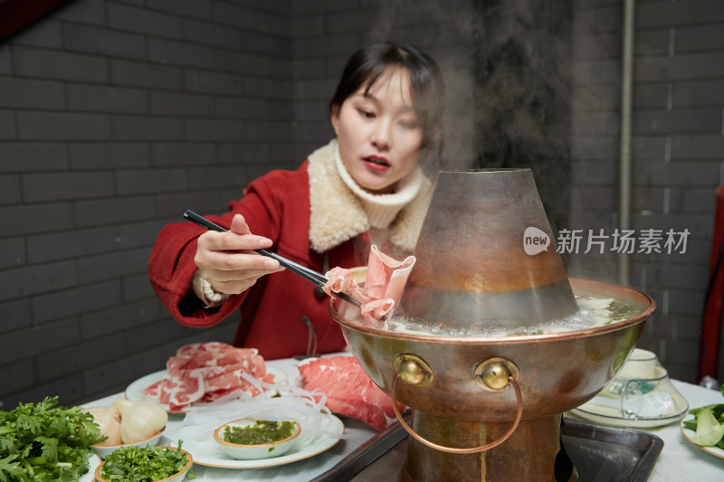 在饭店吃传统铜锅涮肉的亚洲少女