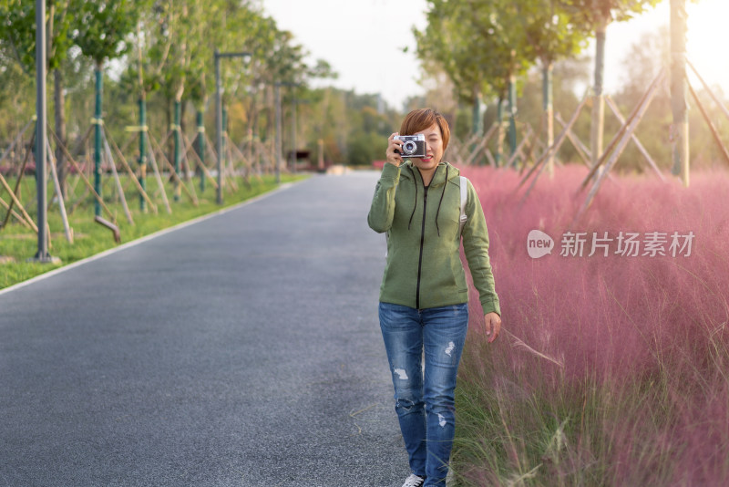年轻的女性用相机在公园的花丛前拍照