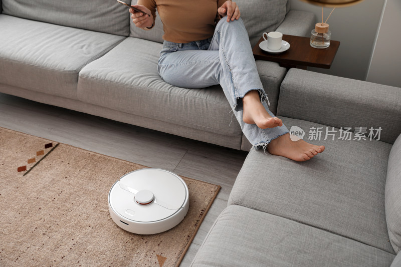 女子沙发上玩手机与扫地机器人