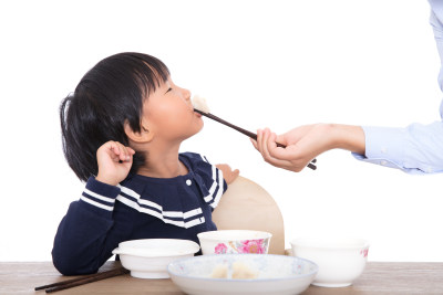 白背景前的餐桌上妈妈在喂孩子吃饺子