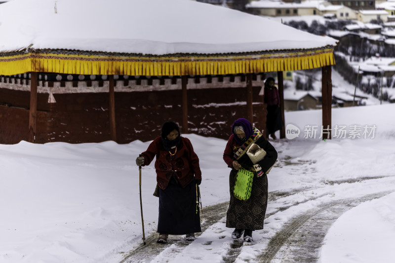 雪地中拄拐行走的藏族老年女性