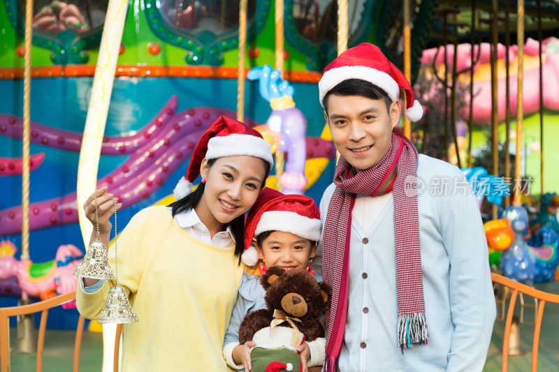 快乐的一家三口戴着圣诞帽在游乐园玩