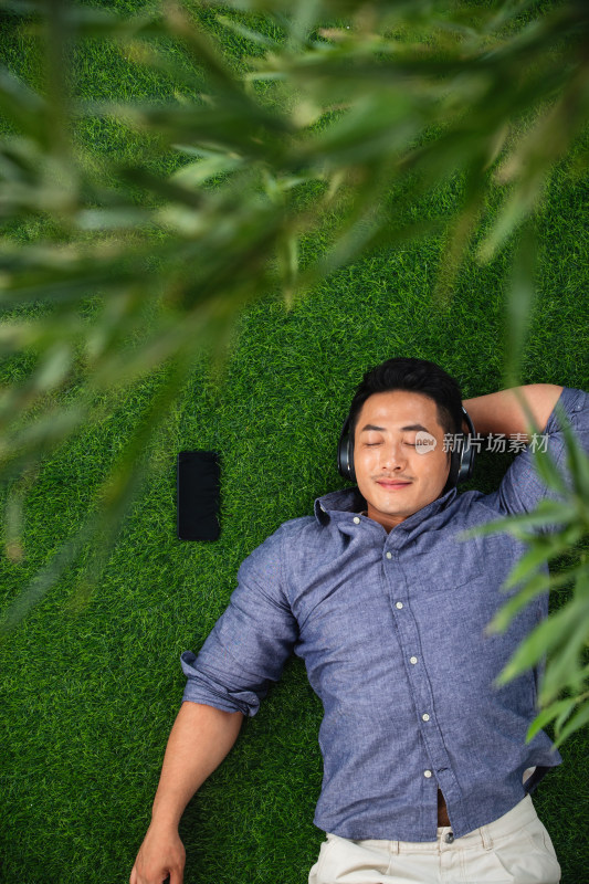 躺在草地上听音乐的青年男人