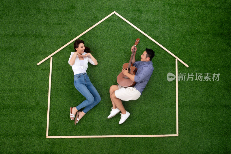 青年伴侣躺在草地上的房子轮廓里唱歌跳舞