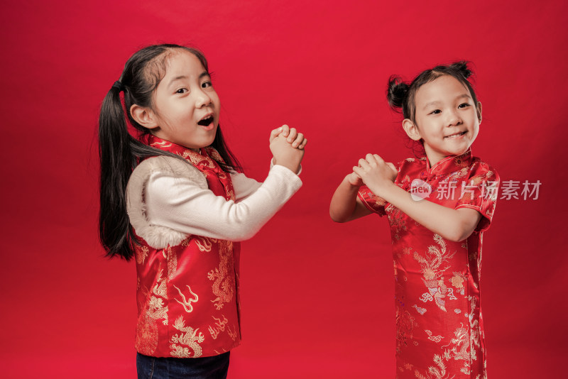 两个站在红色背景前穿唐装作揖的中国女孩
