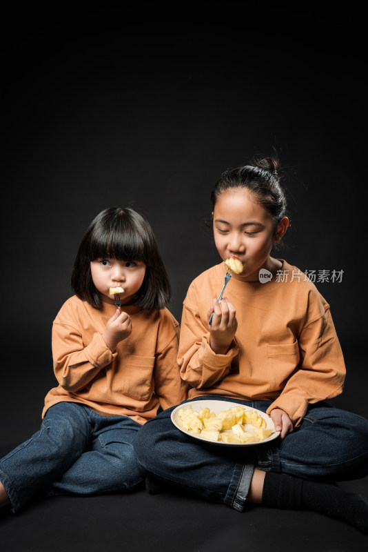 坐在黑背景前吃水果的两个亚裔女孩