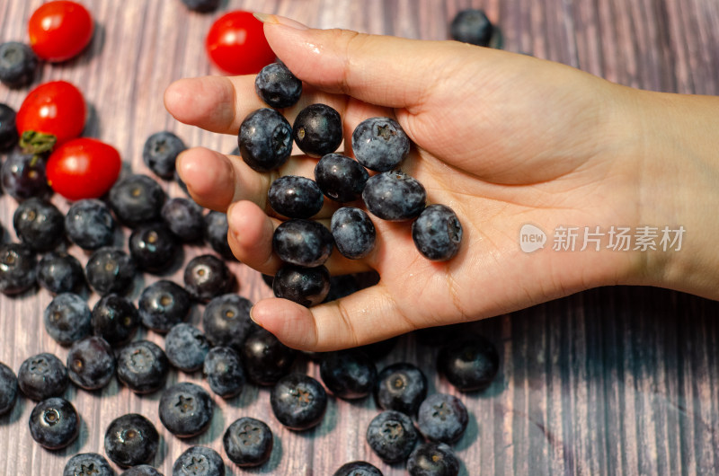 手中捧着蓝莓散落在木质桌面的场景