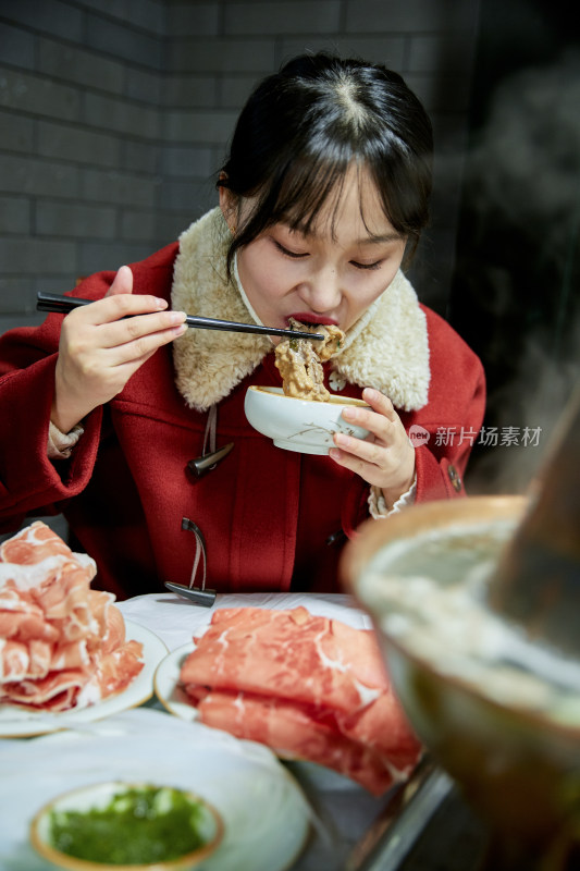 在饭店吃传统铜锅涮肉的亚洲少女