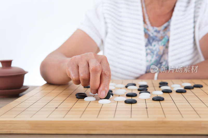 白背景前桌子旁老太太在下围棋