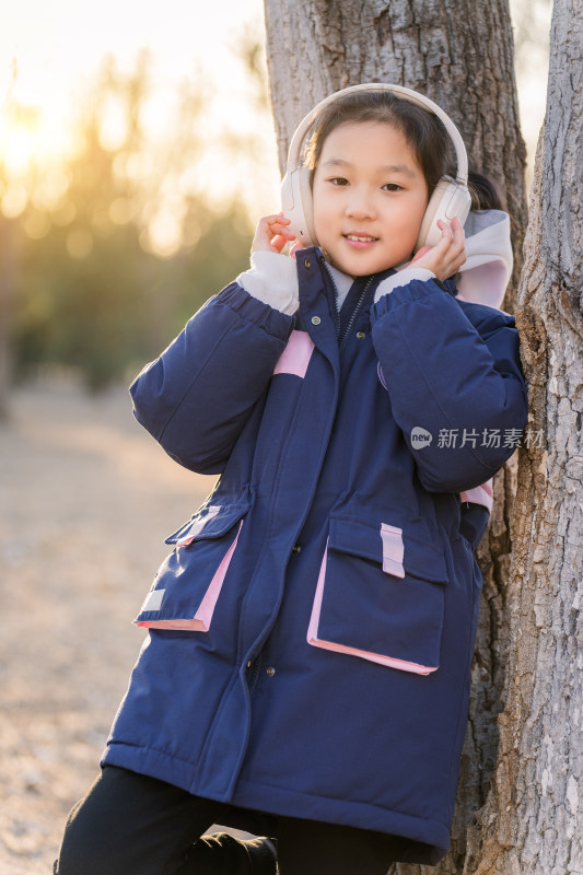 冬日暖阳在公园树林中带耳机欣赏音乐的女孩