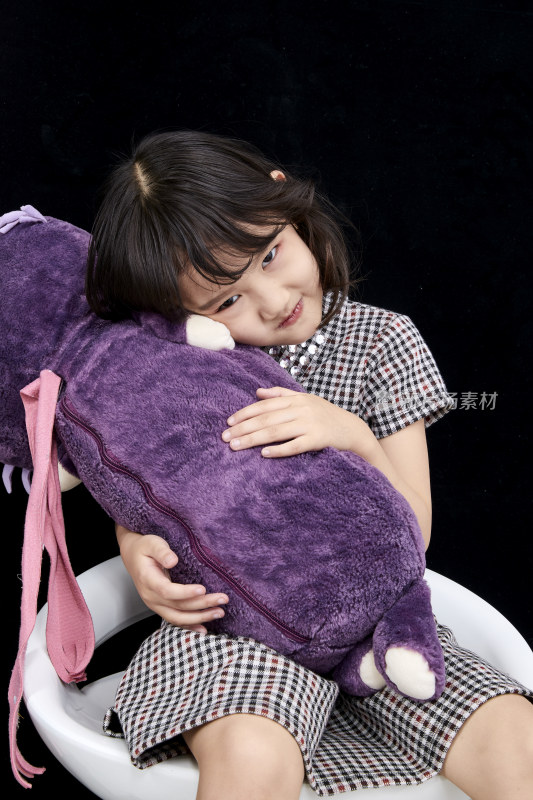 黑色背景里坐在凳子上抱着娃娃玩耍的可爱亚洲小女孩（儿童）