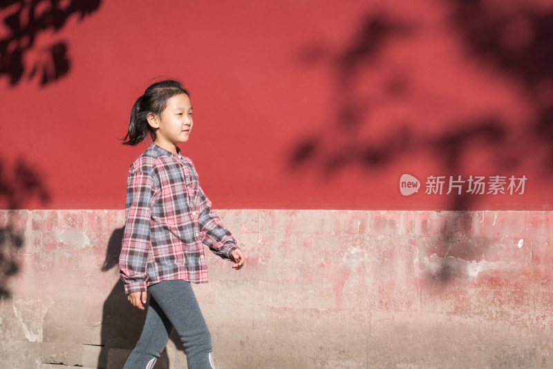 在公园红色围墙下走过的中国女孩
