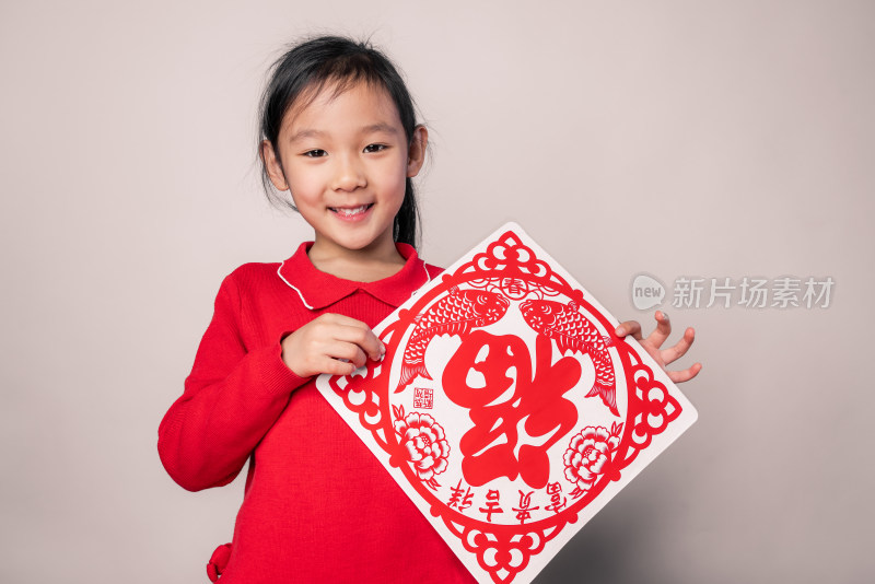 在白色背景前展示剪纸窗花的中国女孩