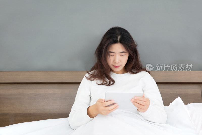 年轻漂亮的女性坐在床上看iPad