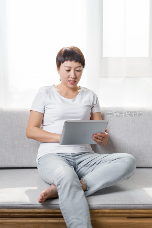 中国女性坐在沙发上使用平板电脑