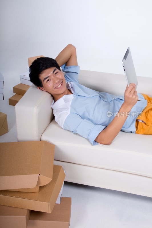 棚拍年轻男人躺在沙发上玩平板电脑
