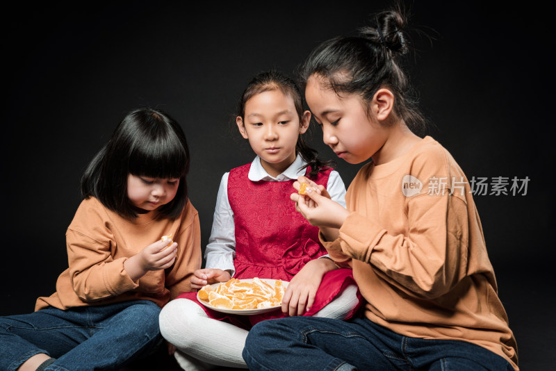 坐在黑背景前吃水果的三个亚裔女孩