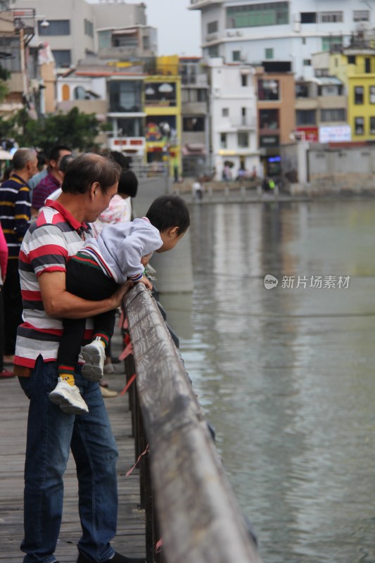 爷爷抱孙子在水边护栏处观望的场景