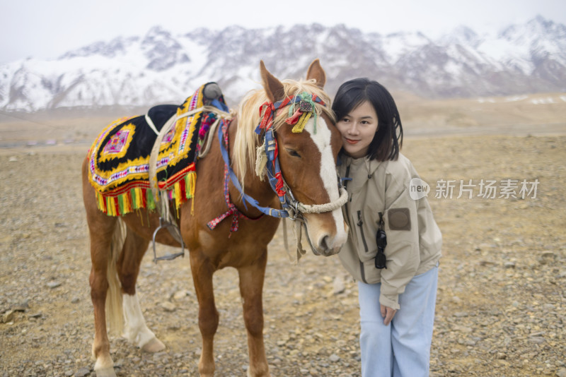 年轻女子在雪山下牵着英俊的马