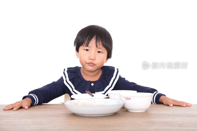 白背景前餐桌旁的小女孩在吃饭